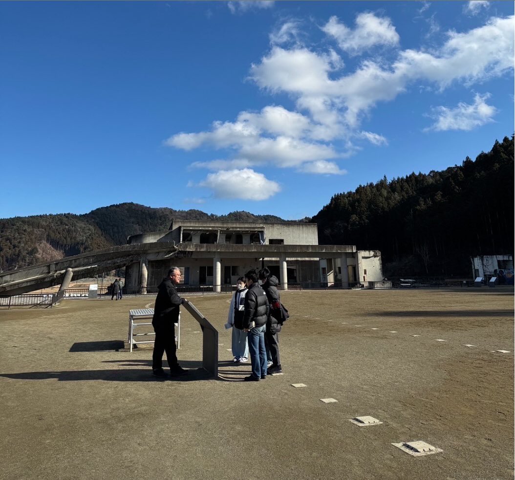※2025年1月にゼミ生（現4年生）は東日本大震災の被災地（石巻・仙台・名取）を訪問し、お話を聞いて回りました。その後就活などで間が空いてしまったのですが、ひとりひとりが印象に残った場所やお話の内容をまとめましたので、少しずつ紹介していきます。

　「ずいぶんと寂しい、何もないところに学校があるな」最初に旧大川小学校を訪れた時の第一印象でした。しかし、あの津波が襲う前には、小学校は周りを住宅に囲まれていて、108人もの生徒が学んでいたと聞き、寂しさがこみ上げると同時に、津波の威力を実感しました。

　語り部の只野英昭さんから、校舎を一望できるグラウンドの真ん中で、被害の様子を説明する看板を前に、説明を聞きました。よく見れば、小学校には珍しい、曲線がたくさん使われた大きくカーブするように建てられた校舎です。

　あの日、津波が迫っているという情報に「山へ逃げよう」と代わる代わる子ども達が言っていたのに、学校側は直前まで全く動かなかった。でも、実際に裏山に行ってみると授業でも使っていたように私たちでも登れるような傾斜でした。

　何度も助かるチャンスがあったのに、どうしてたくさんの命が守れなかったのか、14年近く経っても「本当に何が起きていたのか」を明らかにできない、やるせなさが、只野さんの長いお話から伝わりました。

　今でも、真相を追及し続ける只野さんのエネルギーにも、心を打たれました。裁判の過程で明らかになった避難マニュアルの不備などの問題もあります。私たちも、自分の大切な人の命を守るために、教訓として共有しなければならないことがたくさんあると思いました。＜4年生（当時3年生）池亀廉＞